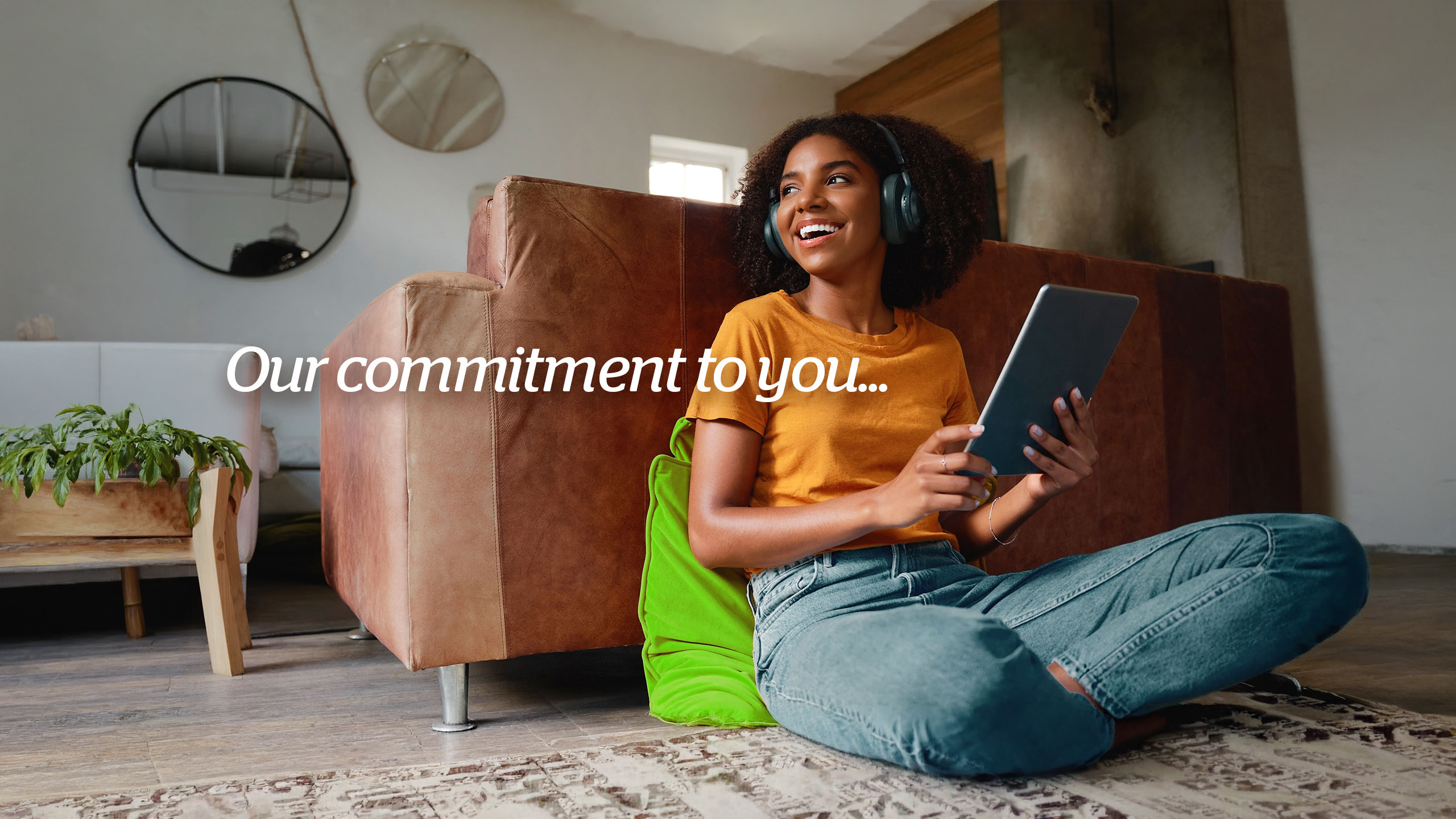 A smiling woman wearing headphones and using a tablet at home
